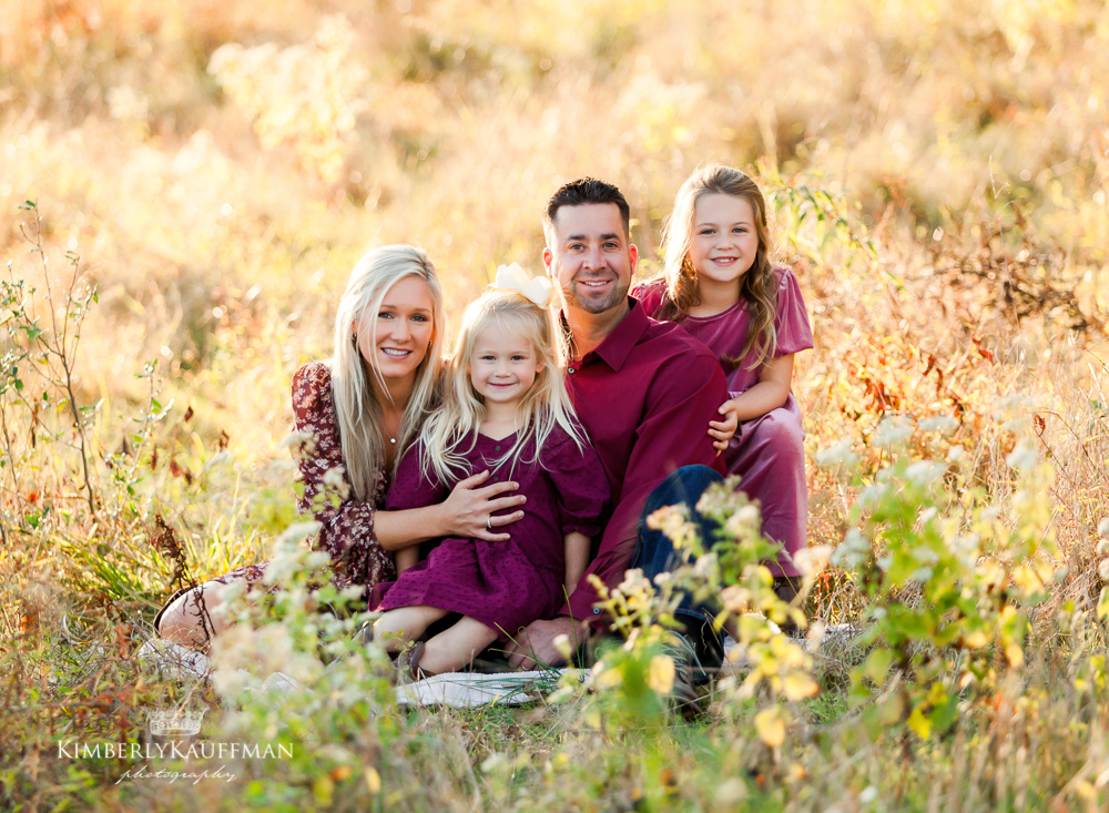 Children sitting between parents on a blanket at golden hour.