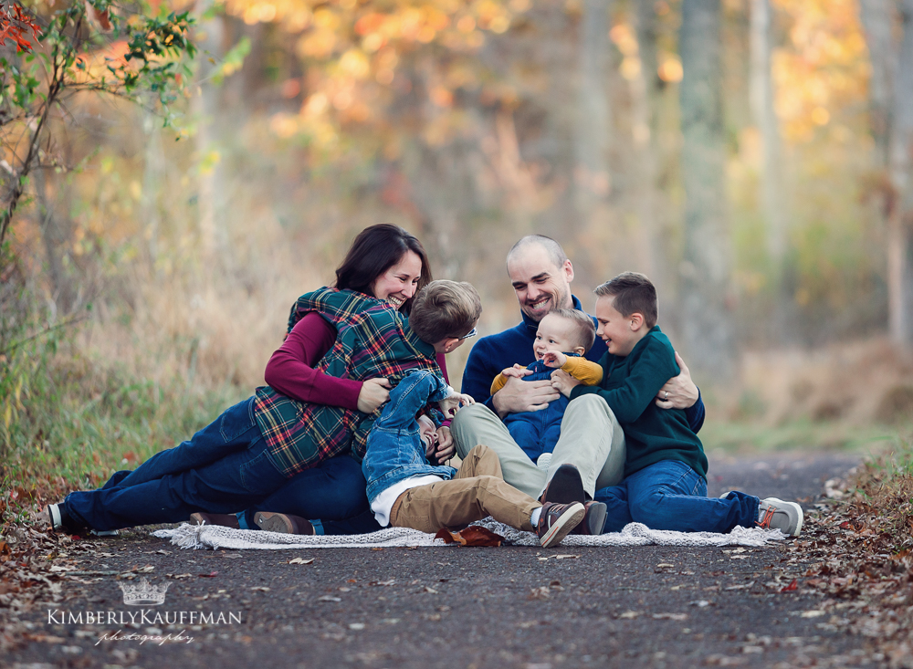 family cuddling close together and laughing with sun flare at golden hour.